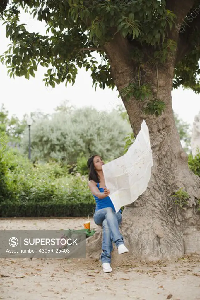 Woman reading map under tree in park