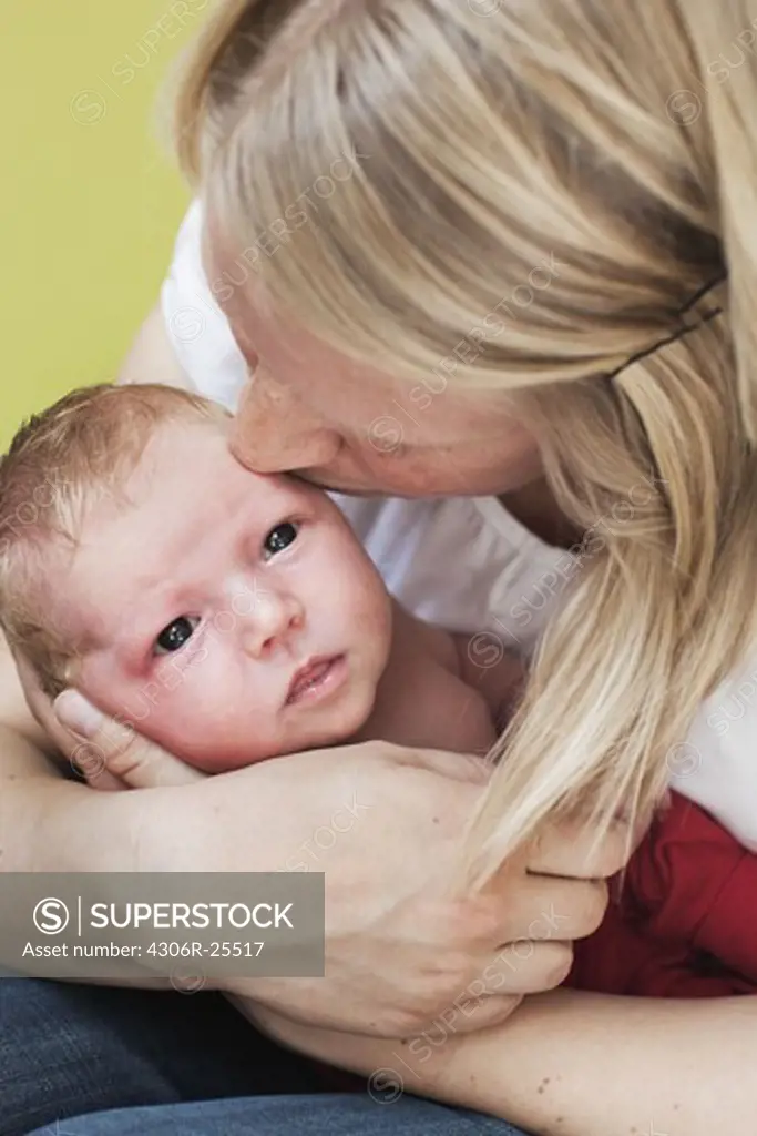 Mid adult woman holding and kissing newborn child