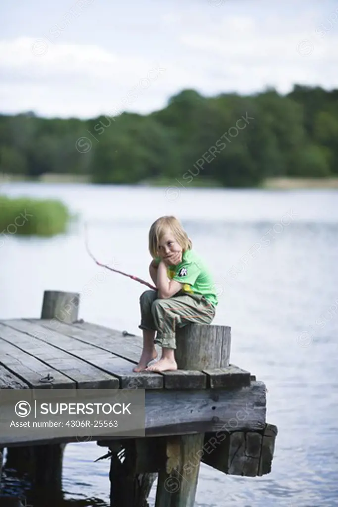 Bored boy sitting on jetty with fishing rod