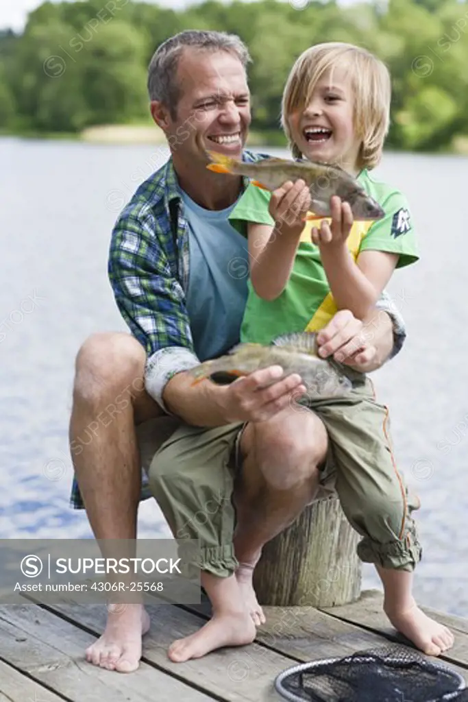 Father and son sitting  on jetty, boy holding fish