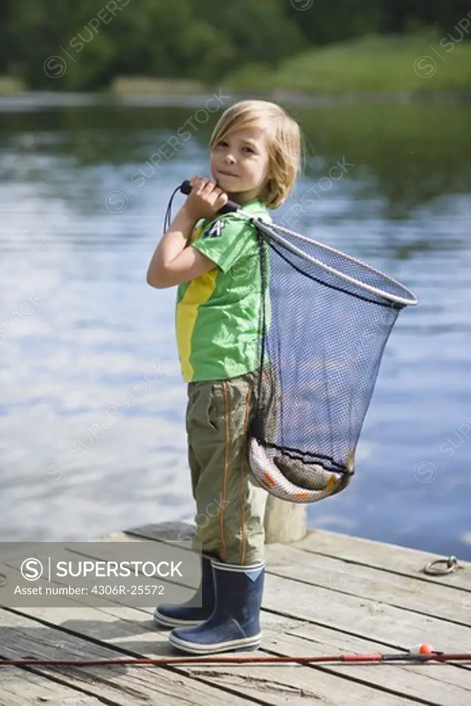 Boy  holding net with catch of fish, standing on jetty