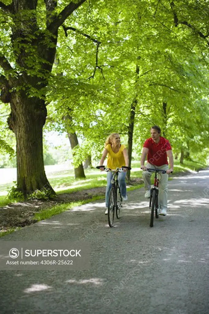 Young couple riding bikes in park