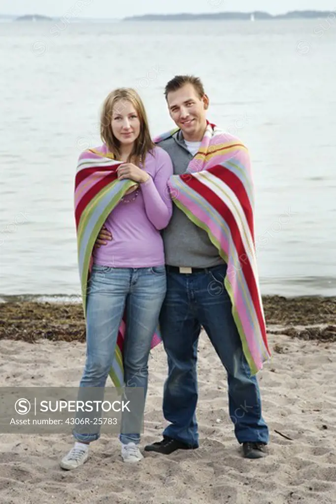 Young couple standing on beach wrapped in blanket
