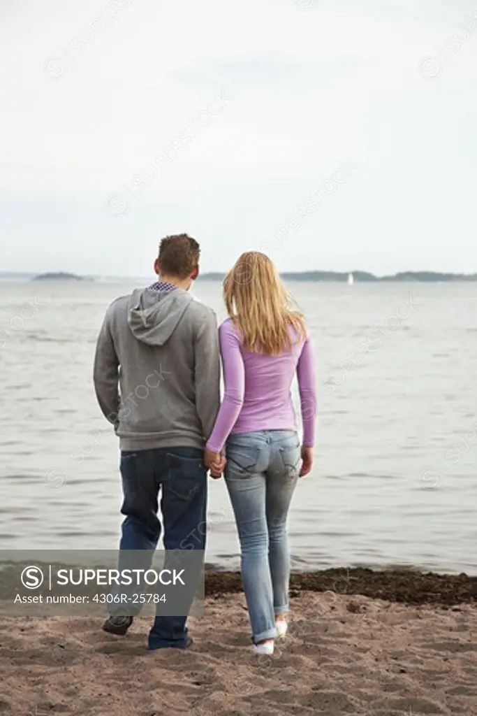 Rear view of couple standing on beach and holding hands