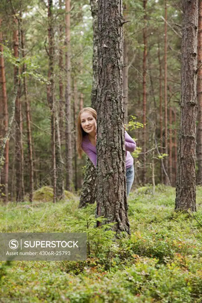 Young woman hiding behind tree in forest