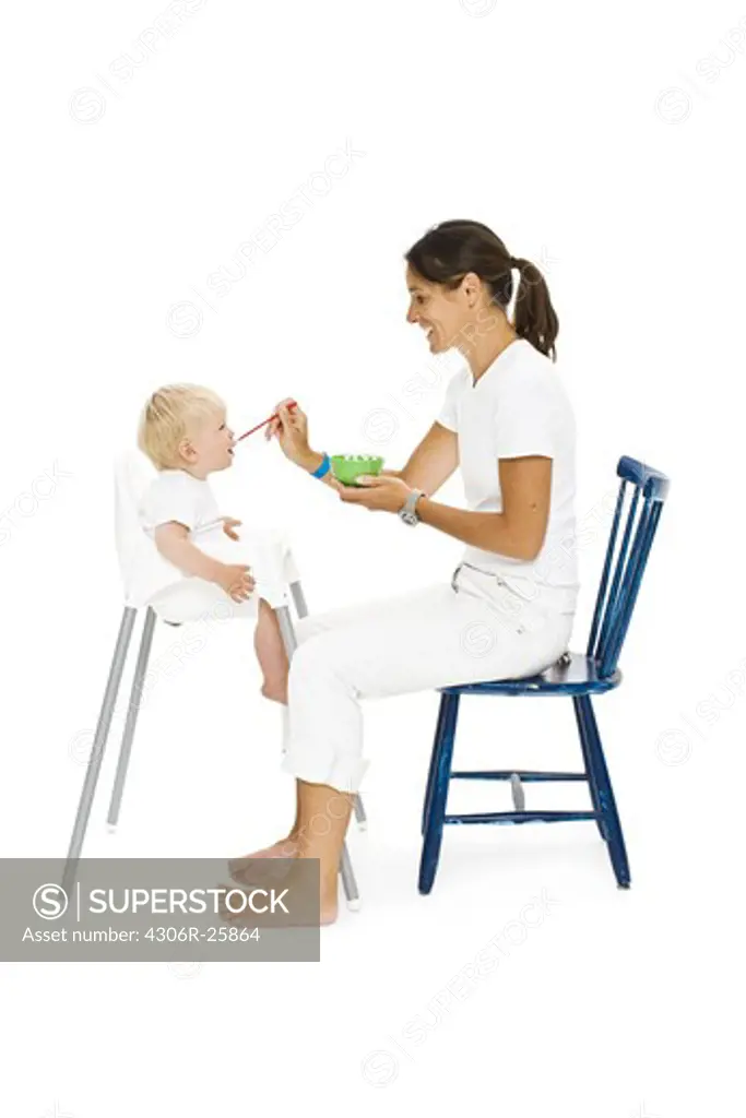 Boy in high chair being fed by mother