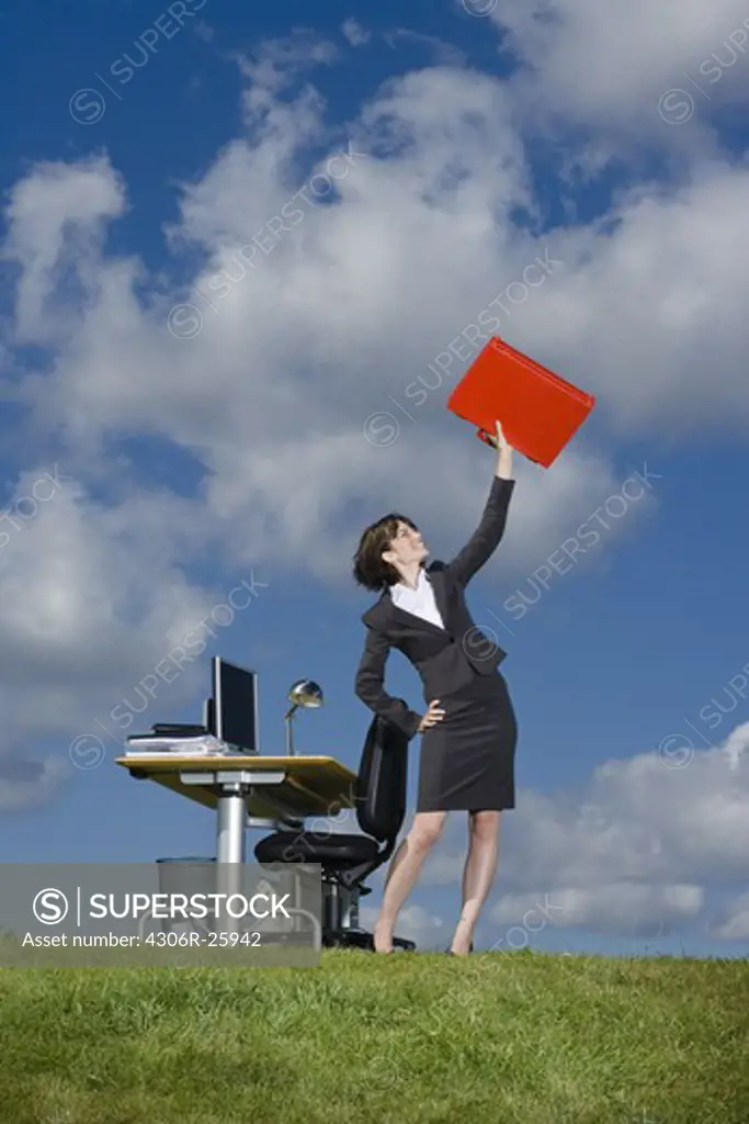 Businesswoman lifting up red briefcase  in grass field