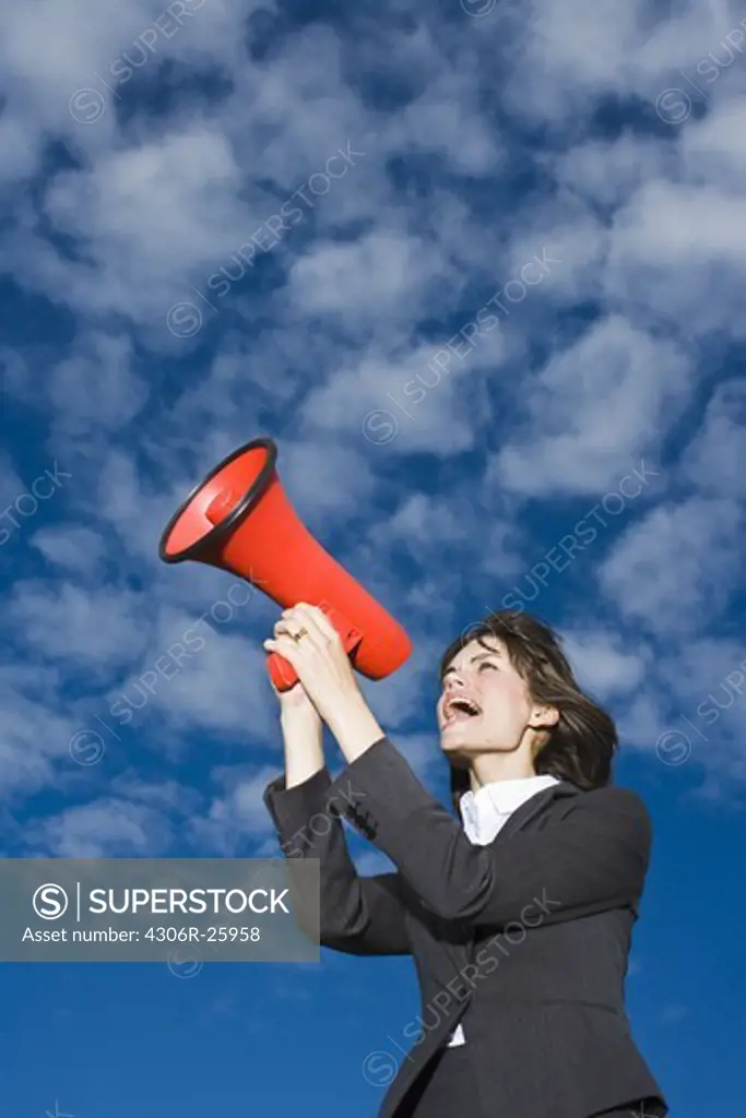 Businesswoman  against blue sky and shouting through red megaphone