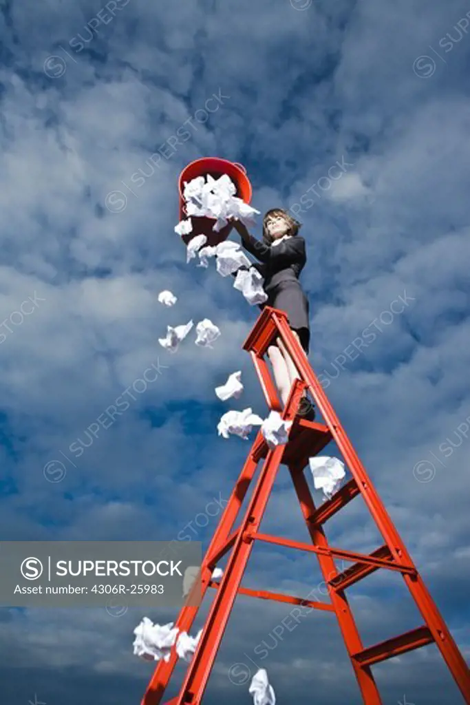 Woman throwing out rubbish from red bin standing on ladder