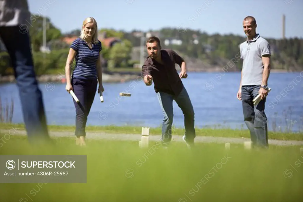 Four adults playing kubb on grass beside sea