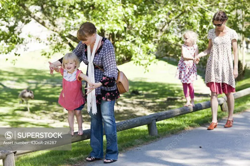 Mothers assisting daughters walking on railing at zoo
