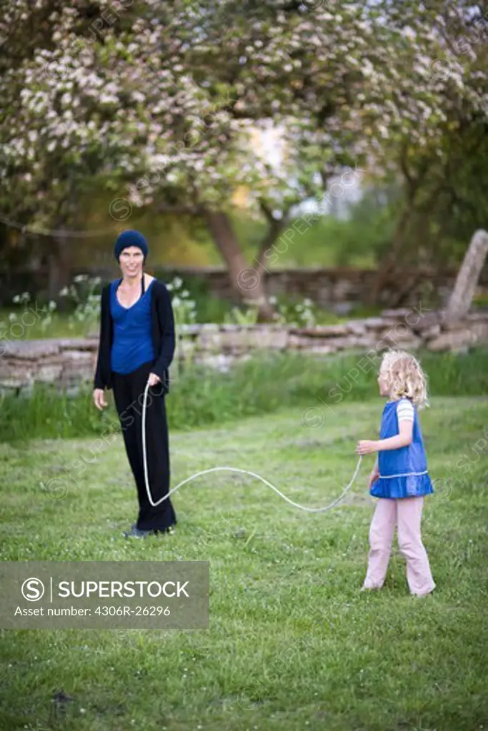 Girl playing with skipping rope in garden with mother