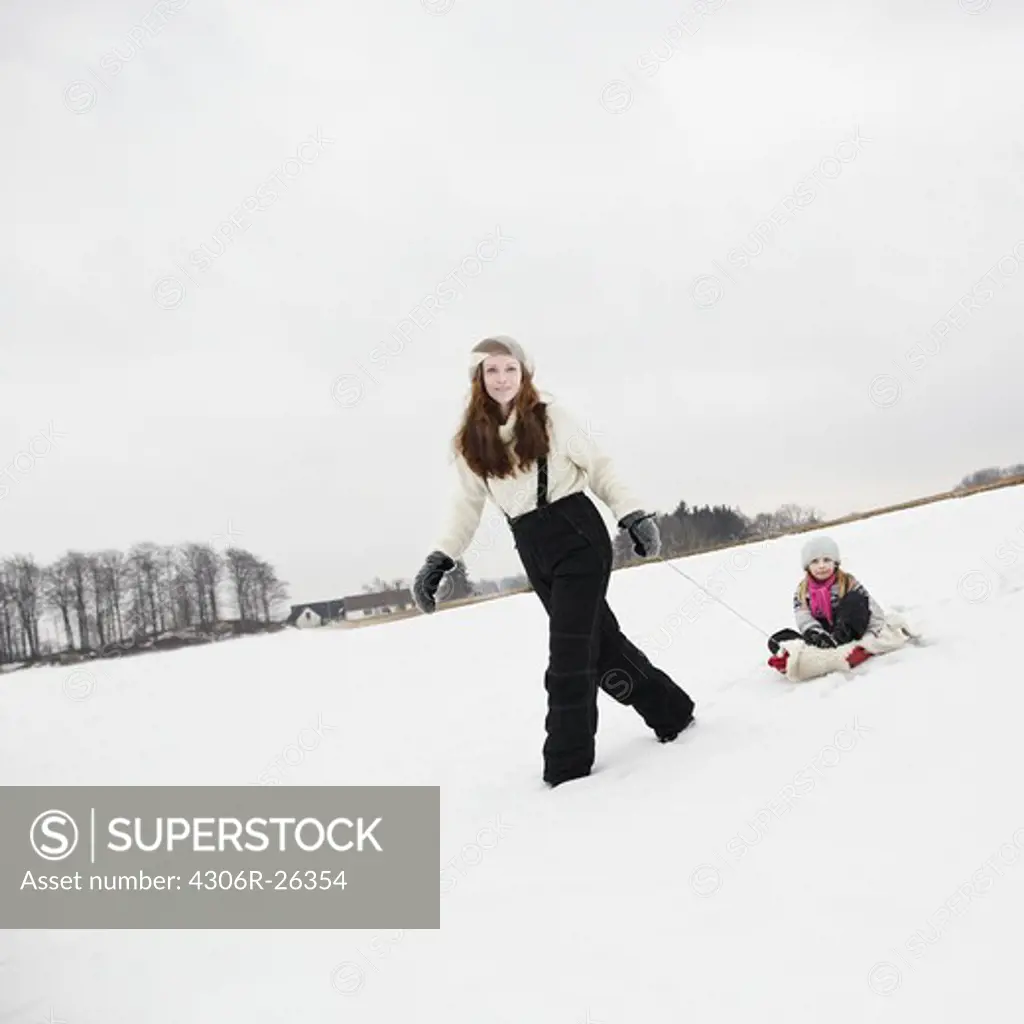 Portrait of mother pulling daughter in sledge