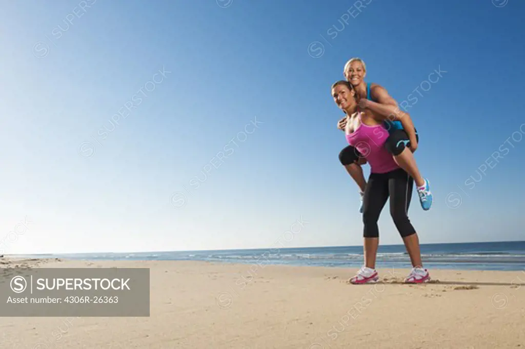 Woman giving friend piggy back on beach