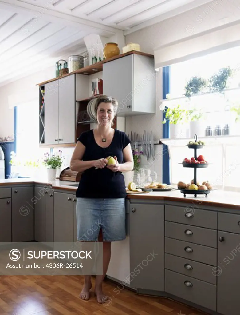 Mature woman standing in kitchen, peeling apple