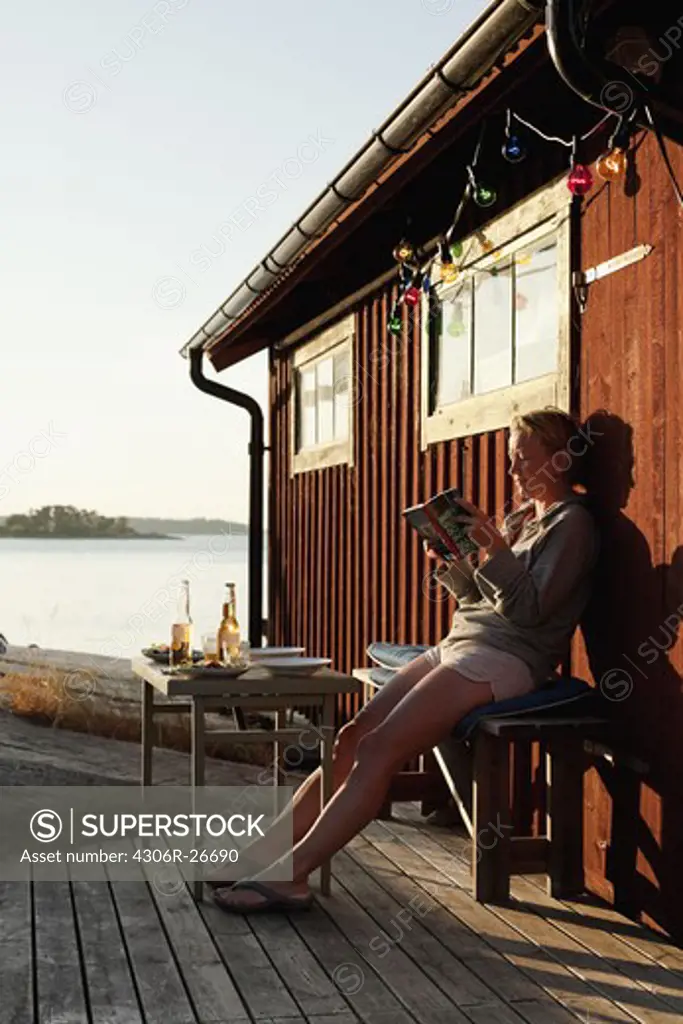 Women sitting by cottage and reading book, sea in background