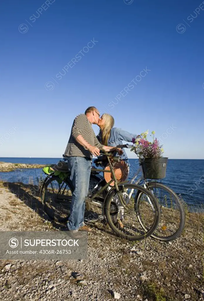 Mature couple riding bicycle on beach and kissing