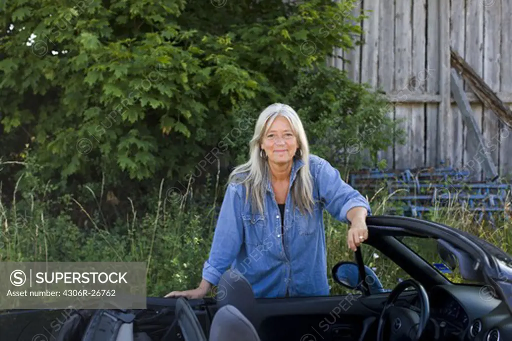 Mature woman standing next to convertible car