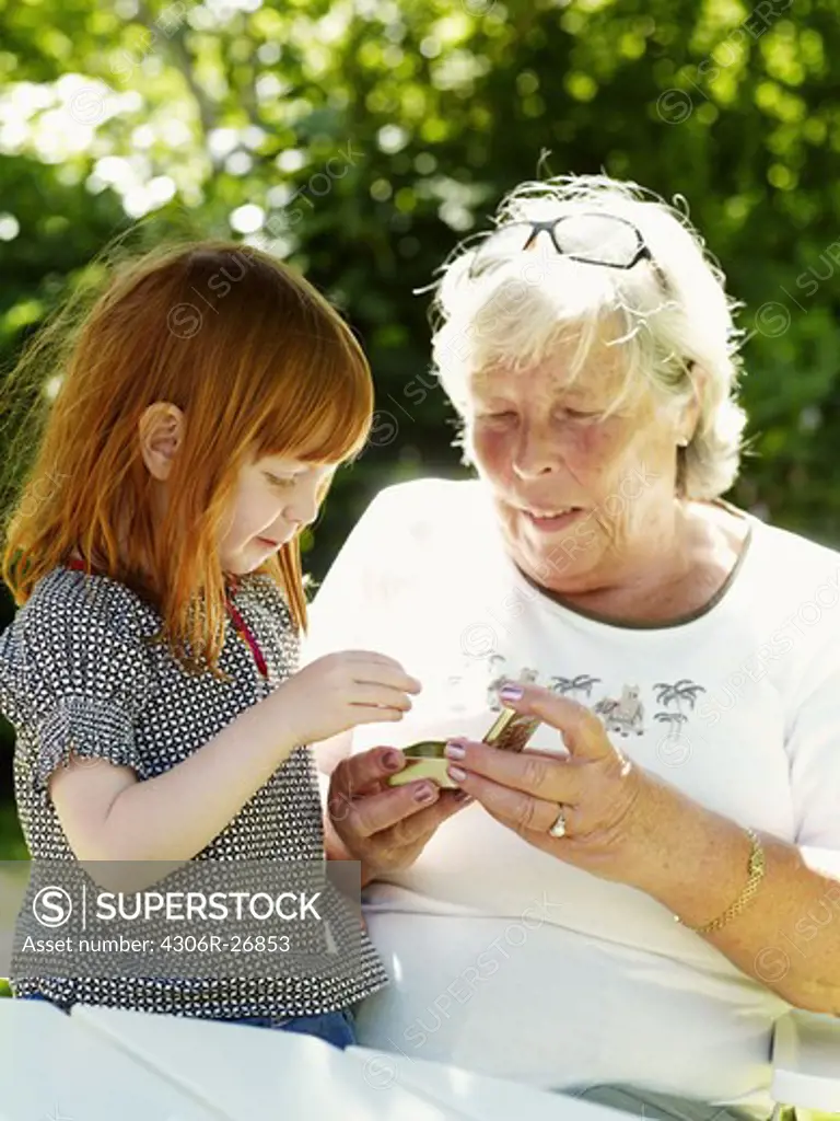 Grandmother and granddaughter eating hard candies in garden