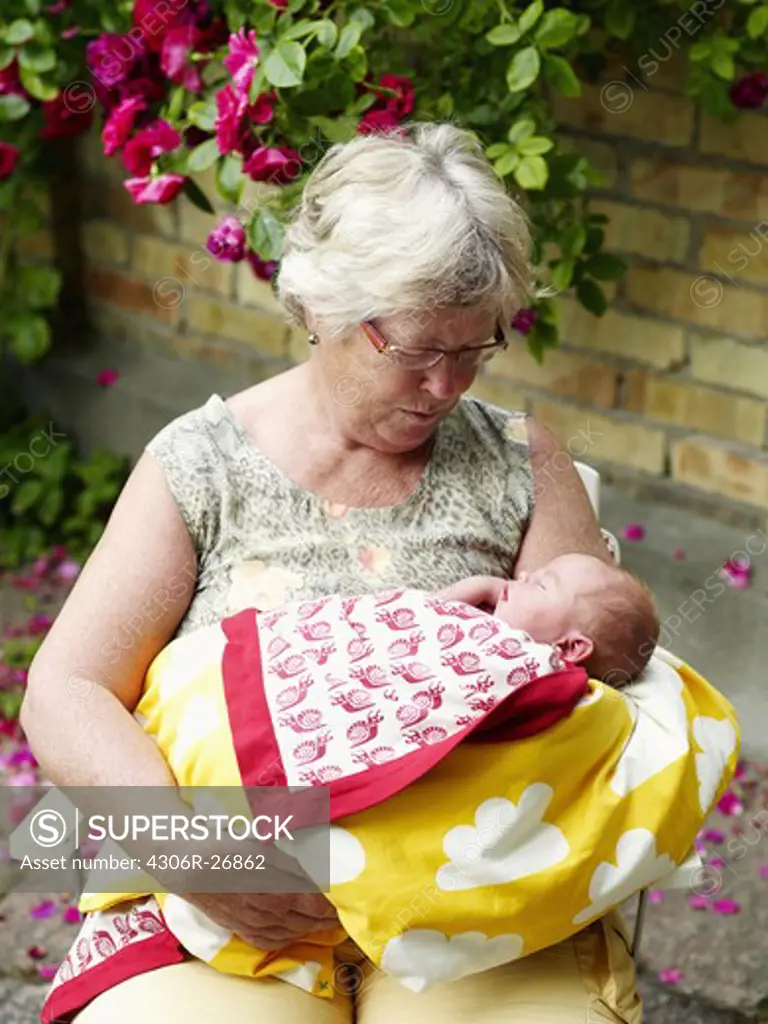 Grandmother sitting in front of house and holding baby