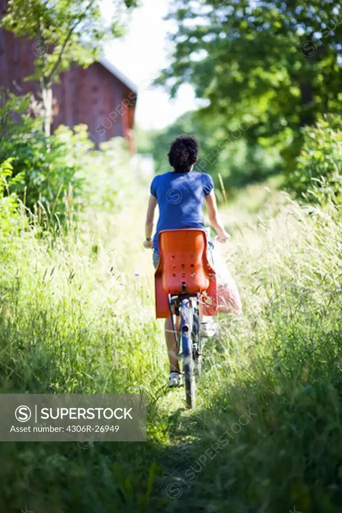 Woman cycling through grass field, rear view