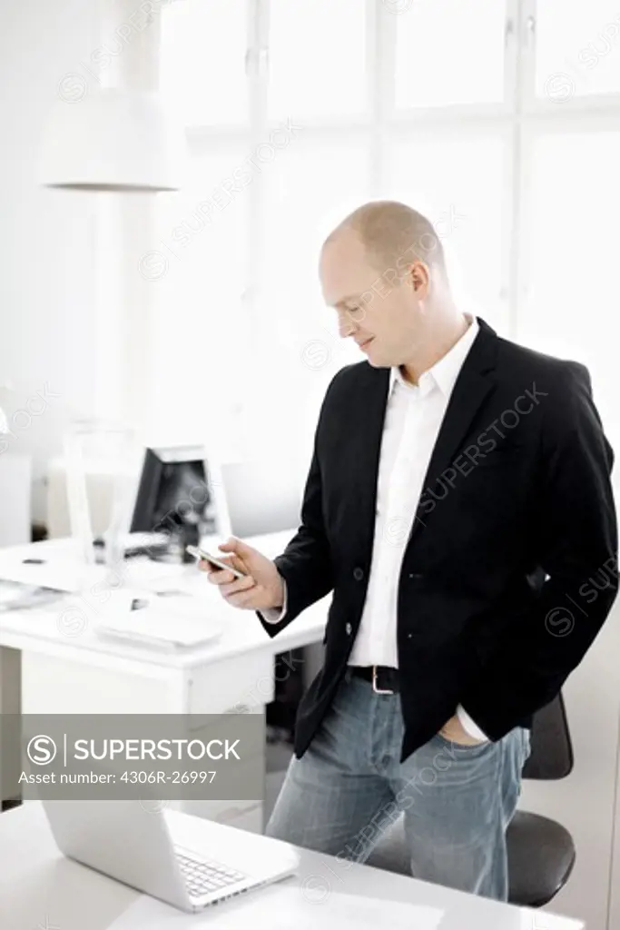 Man standing in office looking mobile phone