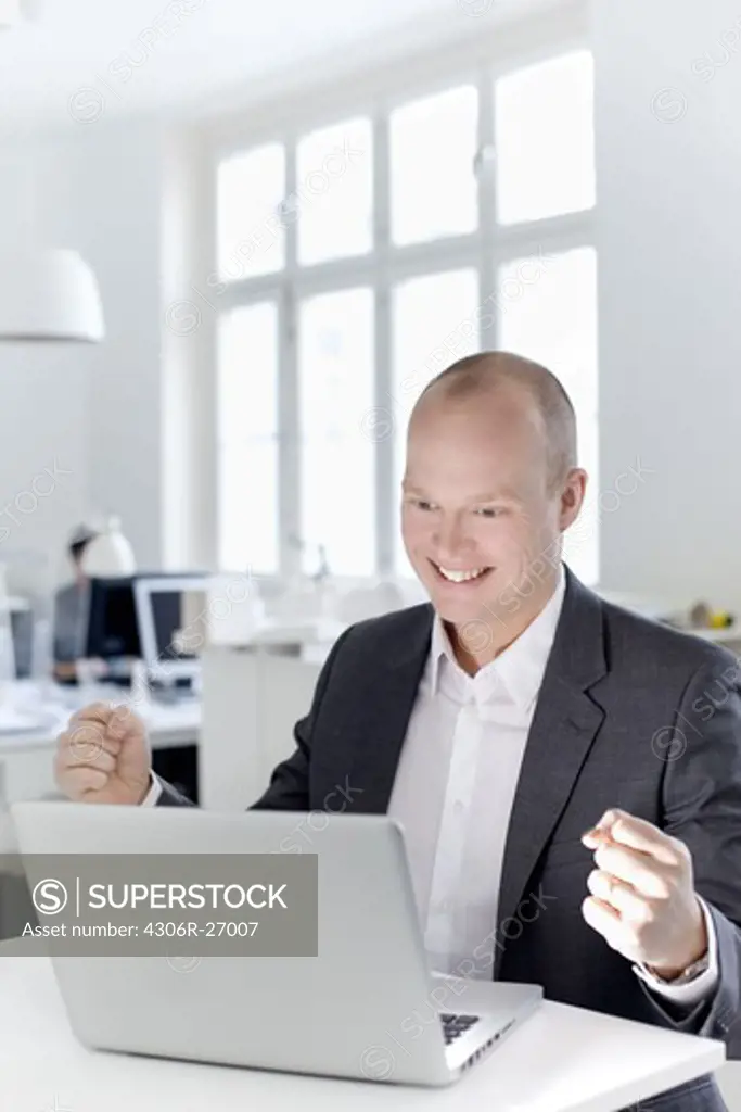 Man looking at laptop and cheering in office