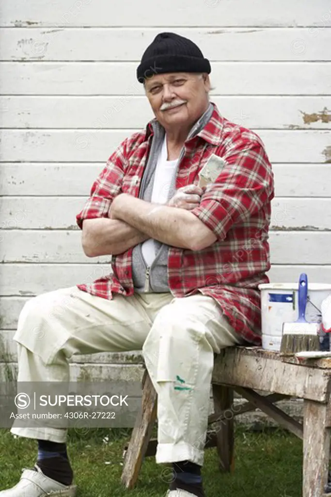 Elderly man painting his summer cottage, Sweden.