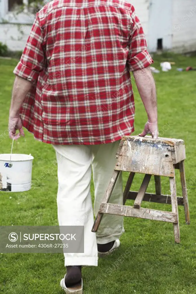 Elderly man painting his summer cottage, Sweden.