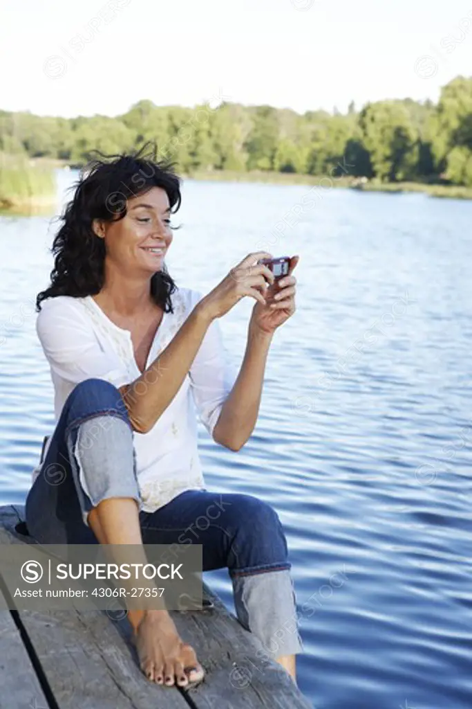 A woman sitting on a jetty using her mobile phone, Sweden.
