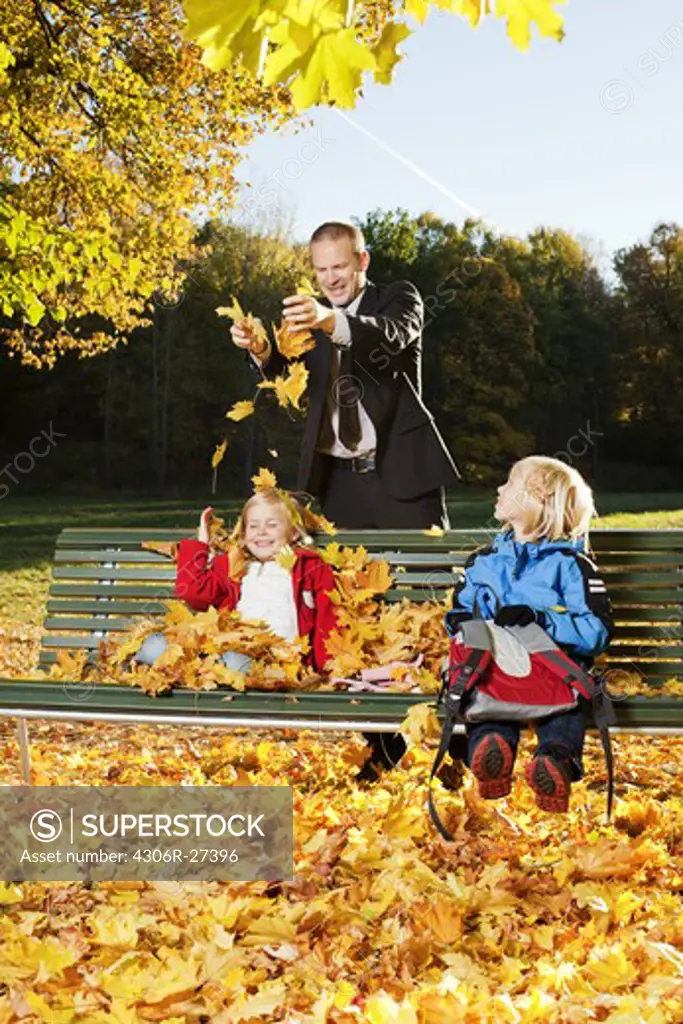 Father and children playing with autumn leaves in park
