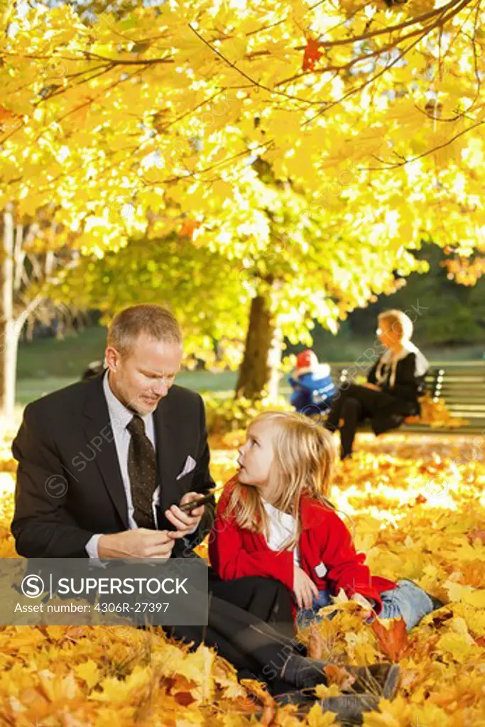 Father and daughter sitting in autumn leaves in park