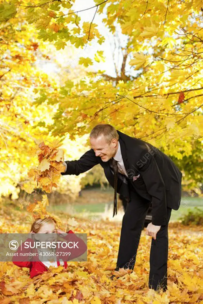 Father and daughter playing with autumn leaves in park