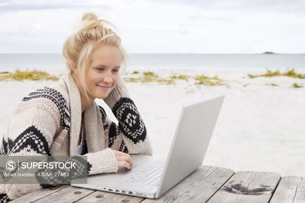 Teenage girl sitting at table, using laptop