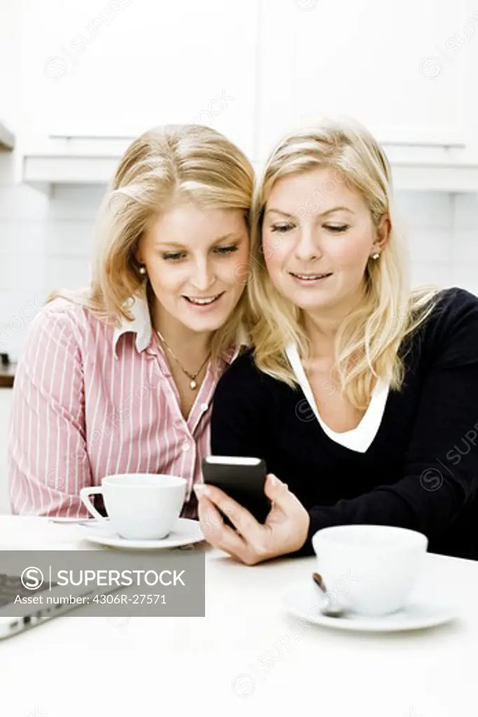 Two young women using mobile phone in kitchen