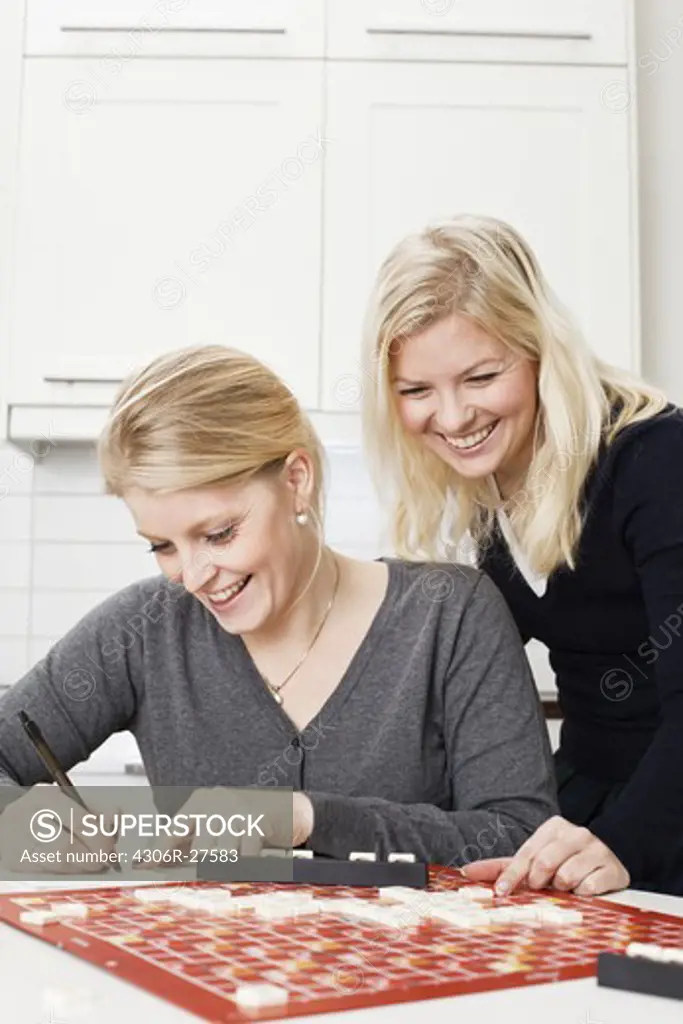 Two young women playing board game in kitchen