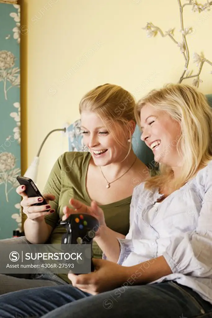 Two young women using mobile phone in bedroom