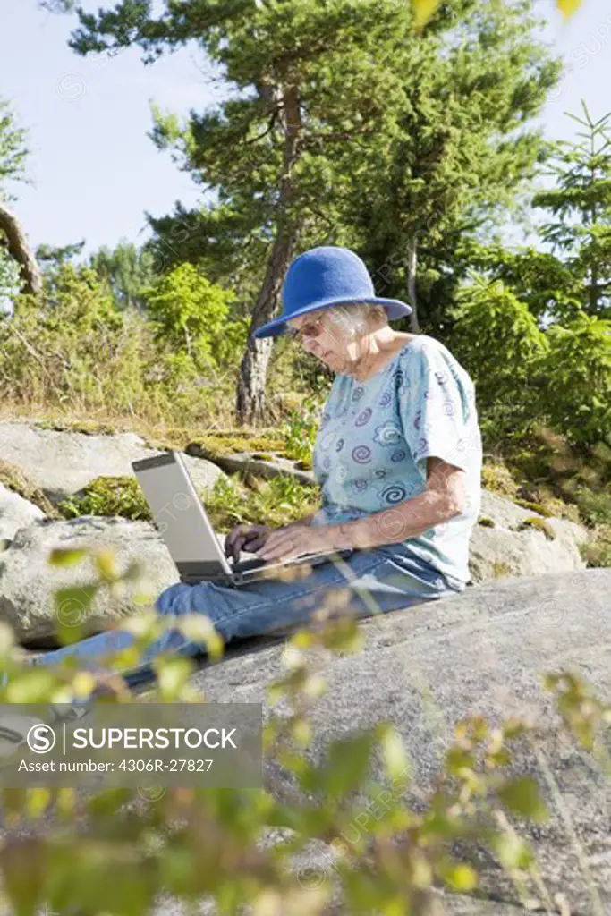 Senior woman sitting on rock using laptop