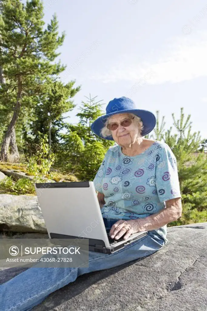 Portrait of senior woman sitting on rock using laptop