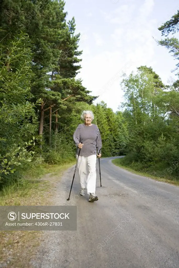 Senior woman walking on country road with hiking poles