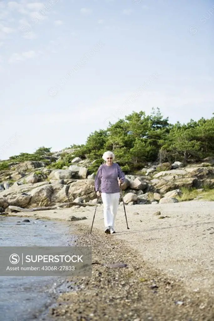Senior woman walking on beach with hiking poles