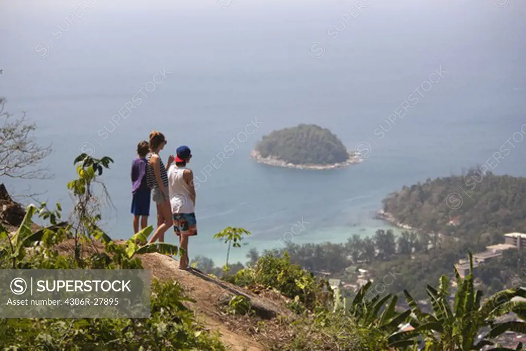 Three teenagers viewing island in sea from cliff