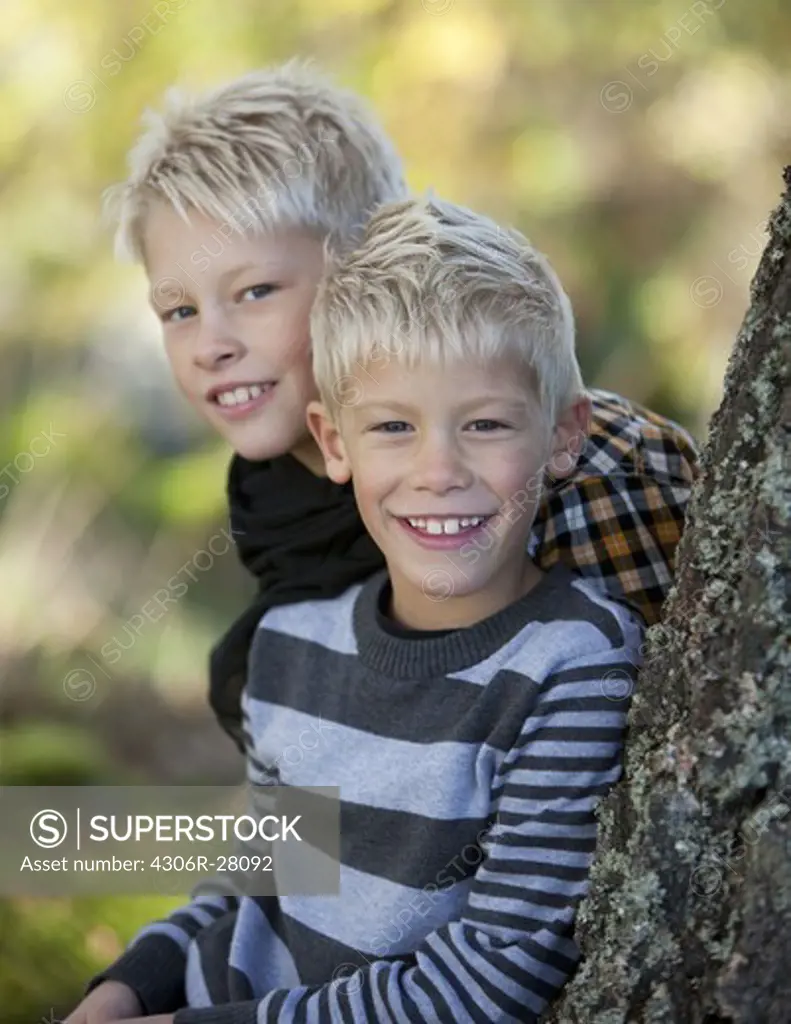 Portrait of two blonde boys leaning against tree trunk