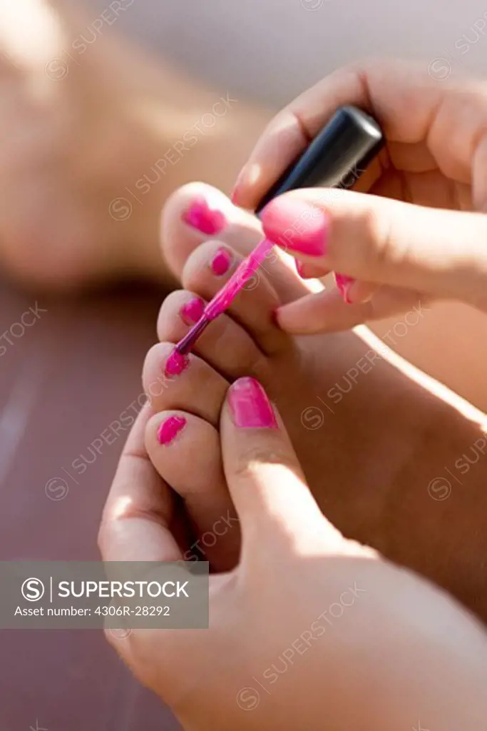 Close up of girls hand painting toenails with pink nail polish
