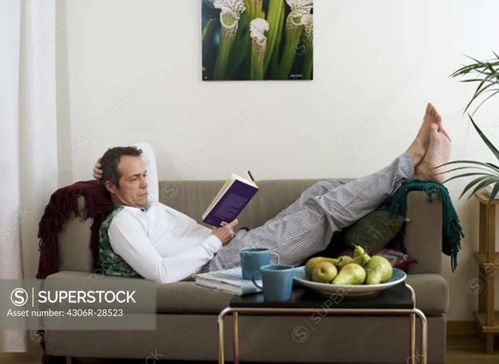 Mid adult man lying on sofa and reading book