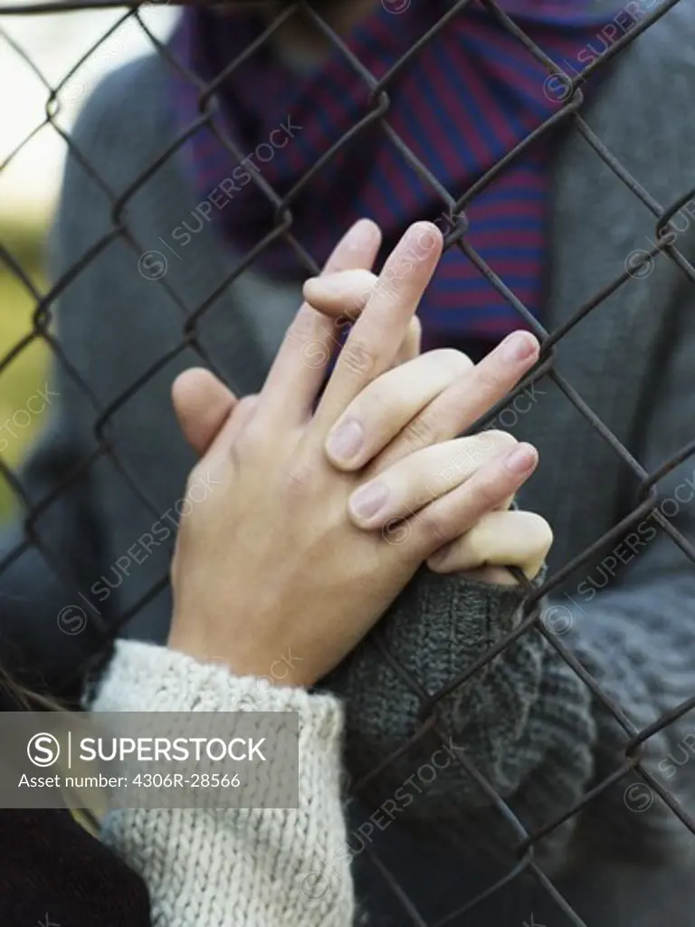Young couple holding hands through wire fence