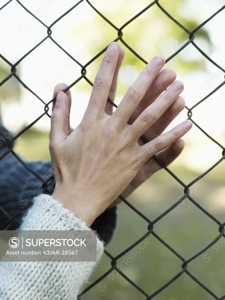 Young couple touching hands through wire fence