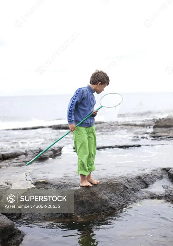 Boy standing on rock by sea holding butterfly net