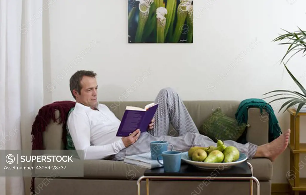 Mature man reading book on sofa