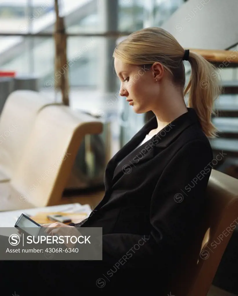 Businesswoman sitting on armchair using personal digital assistant
